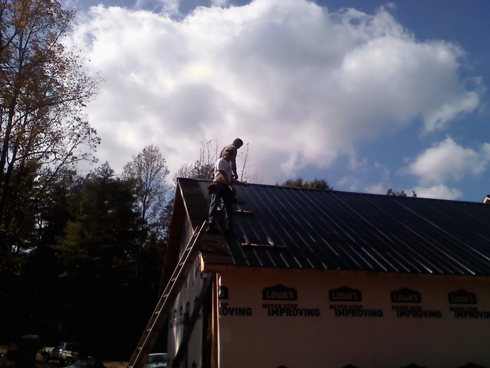 Roofer fastening dark metal panels high against a cloudy sky, from a Roof Inspection job in Parker